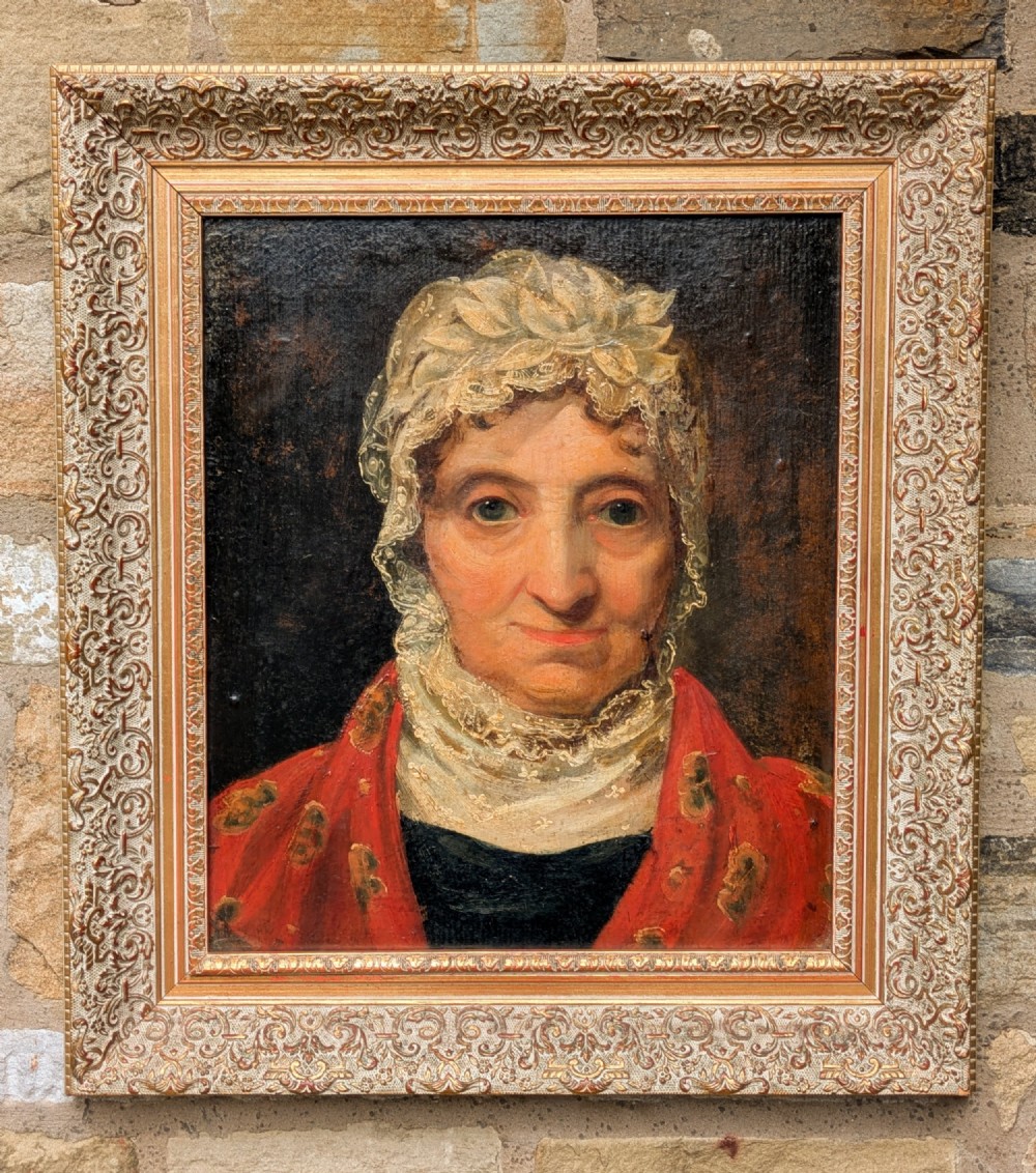 An antique 19th-century oil portrait depicting an elderly woman in a lace cap and red patterned shawl, framed in a carved gilt wood frame.