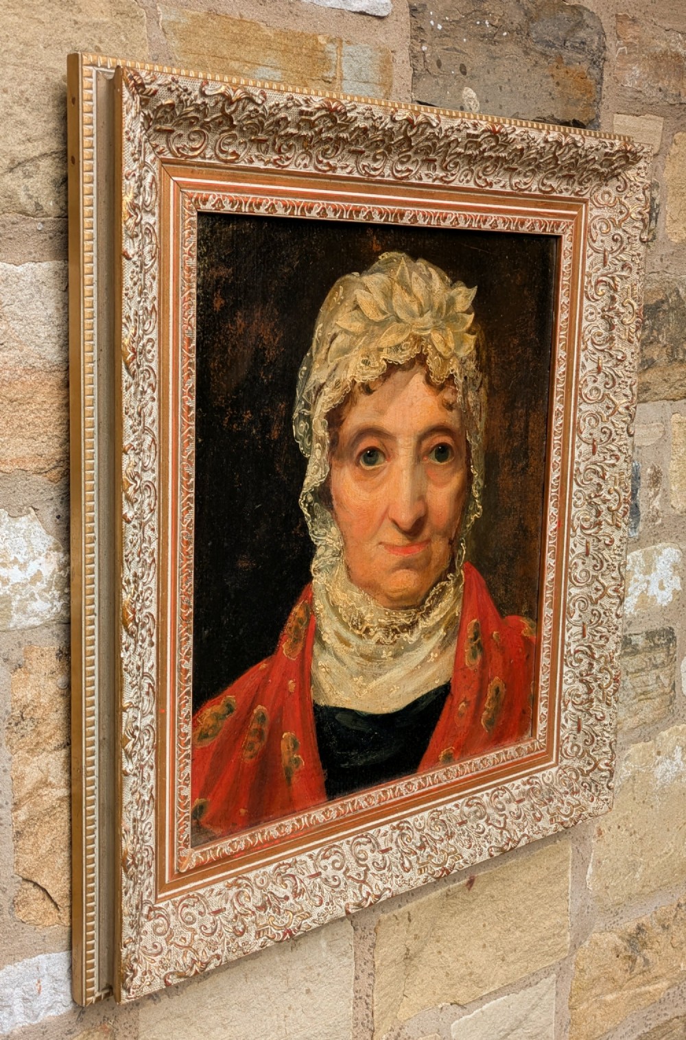 An antique 19th-century oil portrait depicting an elderly woman in a lace cap and red patterned shawl, framed in a carved gilt wood frame. View II