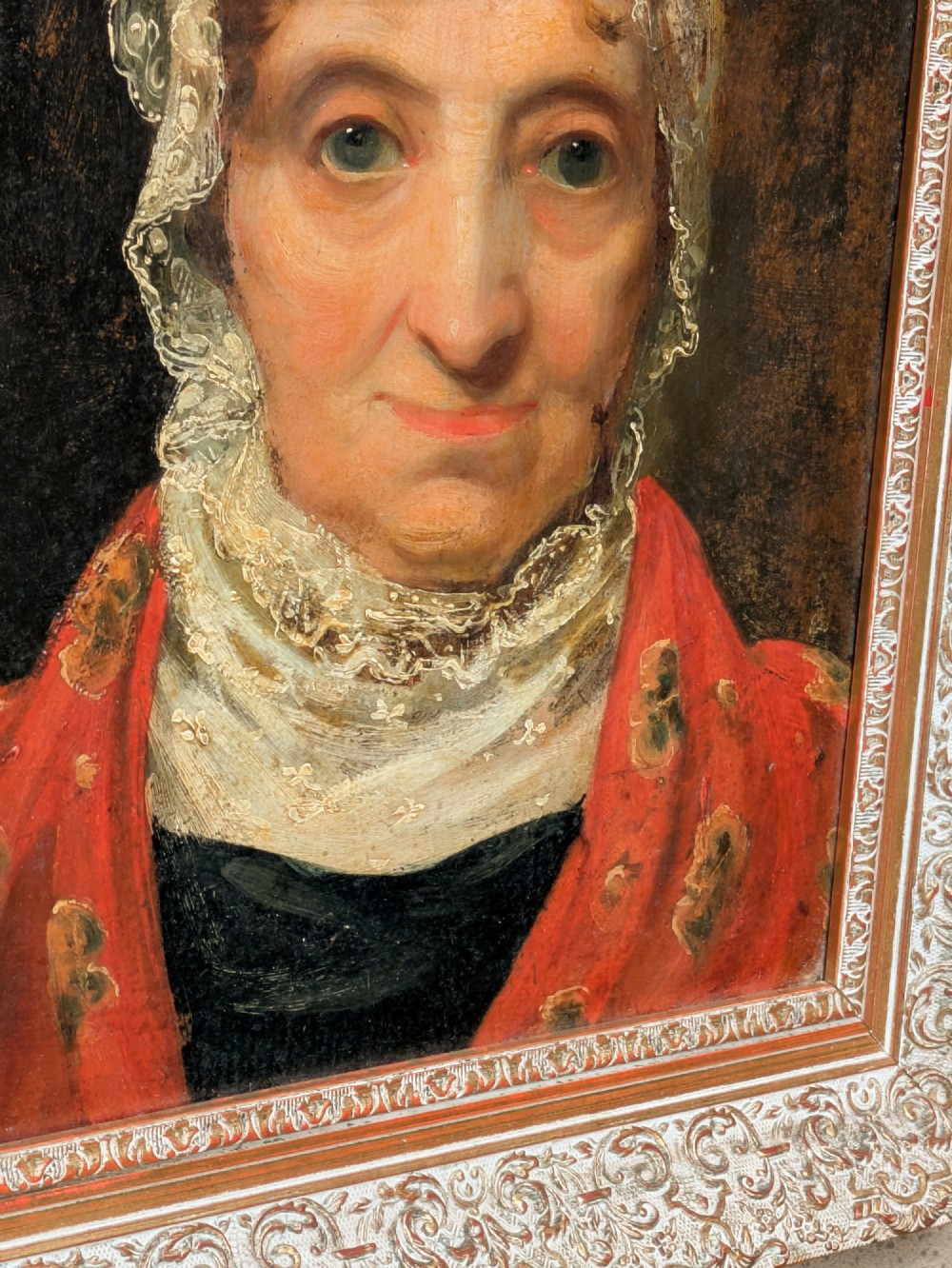 An antique 19th-century oil portrait depicting an elderly woman in a lace cap and red patterned shawl, framed in a carved gilt wood frame. View III
