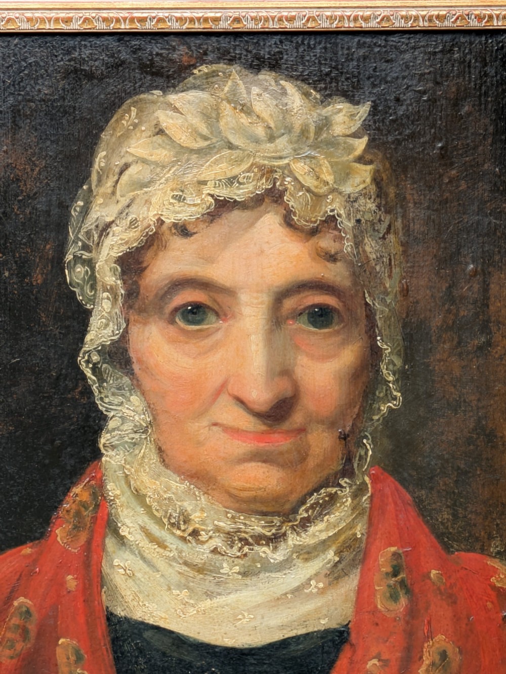 An antique 19th-century oil portrait depicting an elderly woman in a lace cap and red patterned shawl, framed in a carved gilt wood frame. View V