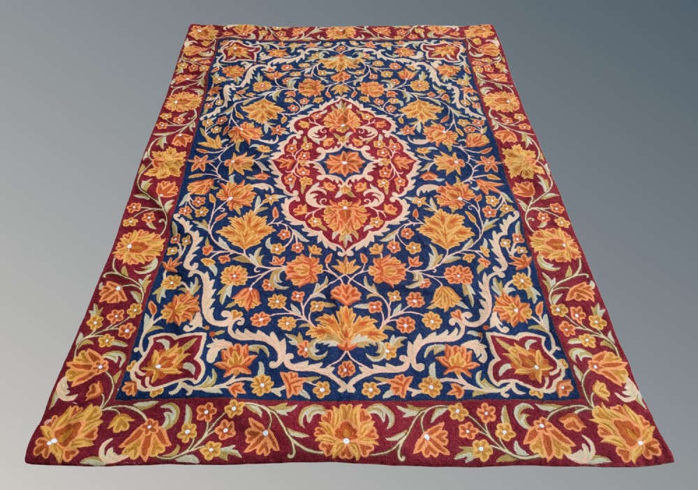 A rectangular Kashmir chain stitch rug featuring dense floral embroidery, a central medallion, and borders in red, navy blue, and gold tones. View II