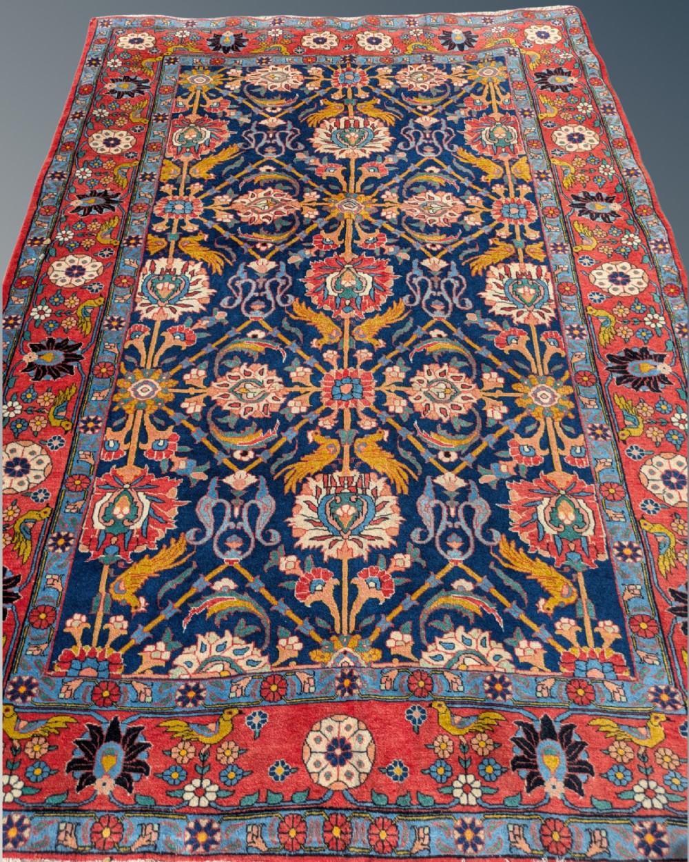 An antique hand-knotted Veramin Persian carpet featuring a dark blue central field filled with a floral lattice pattern and birds, bordered by a wide red band with rosettes. View II