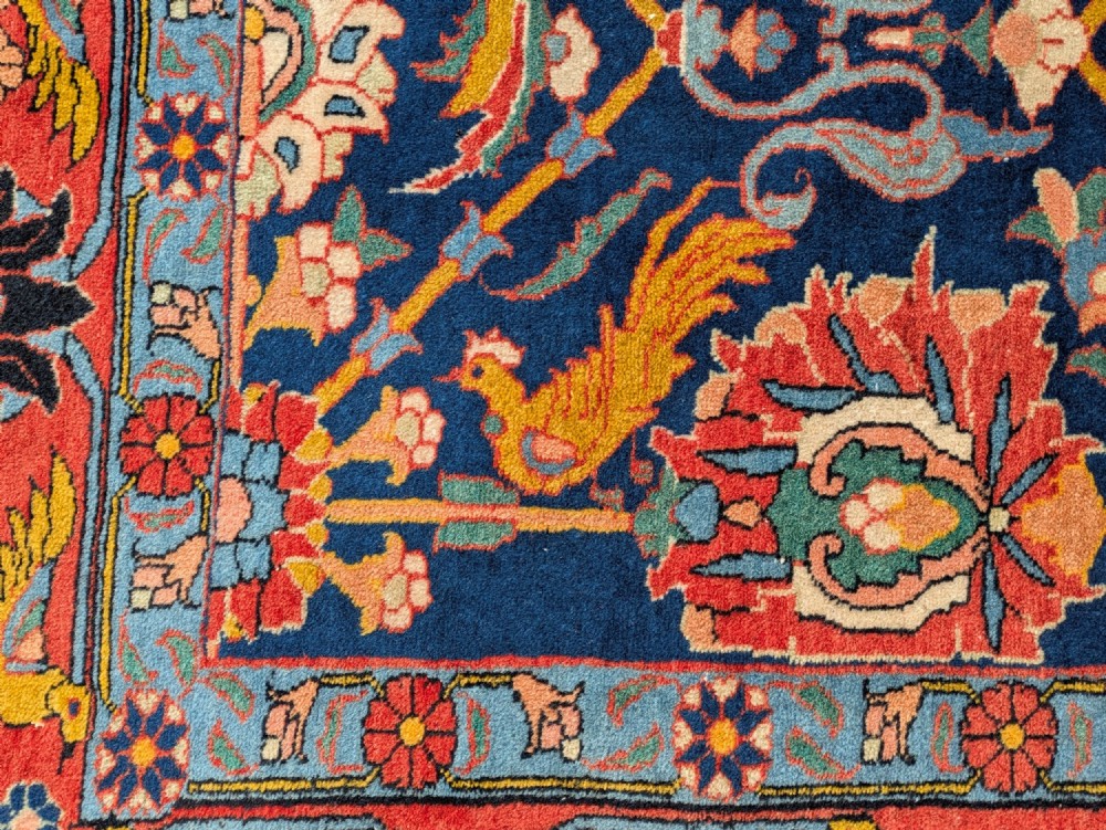 An antique hand-knotted Veramin Persian carpet featuring a dark blue central field filled with a floral lattice pattern and birds, bordered by a wide red band with rosettes. View III