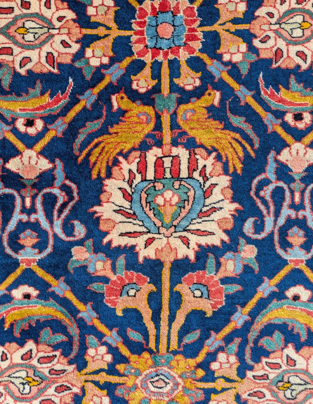 An antique hand-knotted Veramin Persian carpet featuring a dark blue central field filled with a floral lattice pattern and birds, bordered by a wide red band with rosettes. View VI