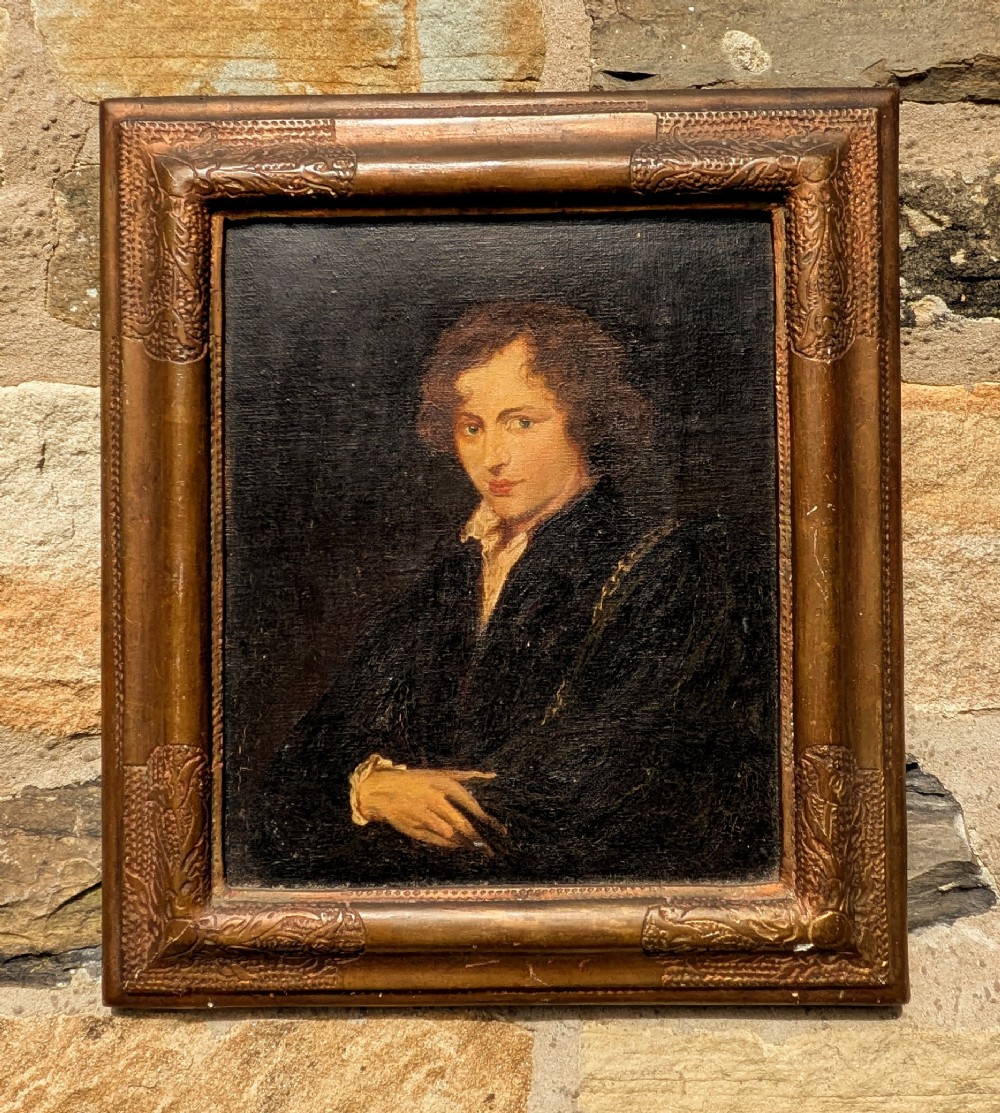 An antique oil painting depicting a young gentleman with dark wavy hair and an open collar set within a decorated metallic gilt frame.