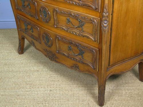 A French walnut chest of drawers featuring three carved drawer fronts, ornate brass handles, a decorative carved apron, and short cabriole legs. View IV