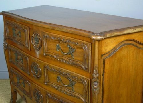 A French walnut chest of drawers featuring three carved drawer fronts, ornate brass handles, a decorative carved apron, and short cabriole legs. View VI