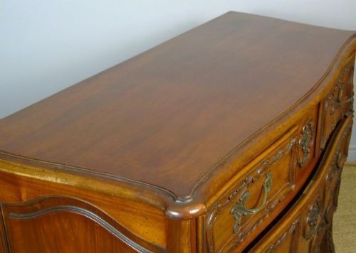 A French walnut chest of drawers featuring three carved drawer fronts, ornate brass handles, a decorative carved apron, and short cabriole legs. View VII