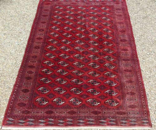 A rectangular hand-knotted wool Tekke carpet featuring repeating octagonal gul motifs across a rich red field surrounded by geometric borders.