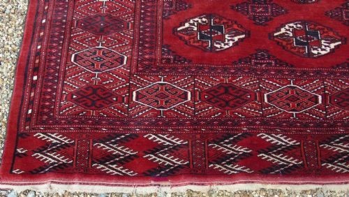 A rectangular hand-knotted wool Tekke carpet featuring repeating octagonal gul motifs across a rich red field surrounded by geometric borders. View III