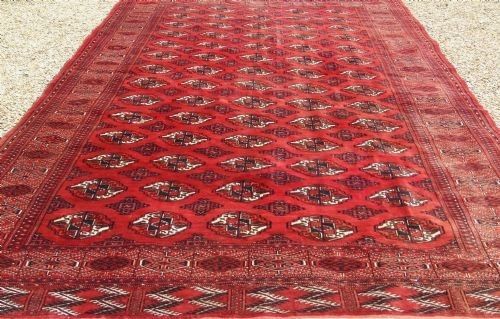 A rectangular hand-knotted wool Tekke carpet featuring repeating octagonal gul motifs across a rich red field surrounded by geometric borders. View IV