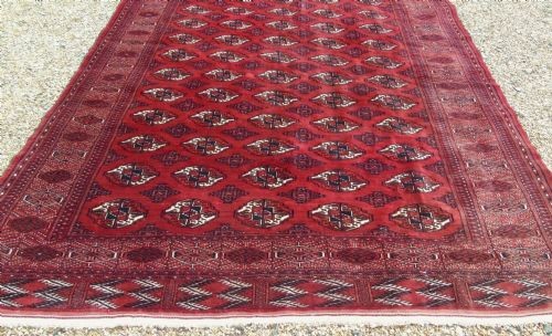 A rectangular hand-knotted wool Tekke carpet featuring repeating octagonal gul motifs across a rich red field surrounded by geometric borders. View V