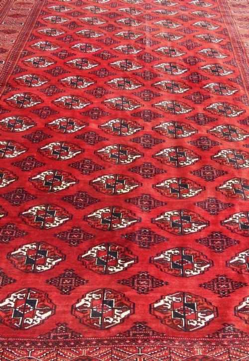 A rectangular hand-knotted wool Tekke carpet featuring repeating octagonal gul motifs across a rich red field surrounded by geometric borders. View VI