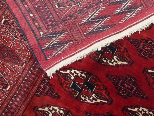 A rectangular hand-knotted wool Tekke carpet featuring repeating octagonal gul motifs across a rich red field surrounded by geometric borders. View VII