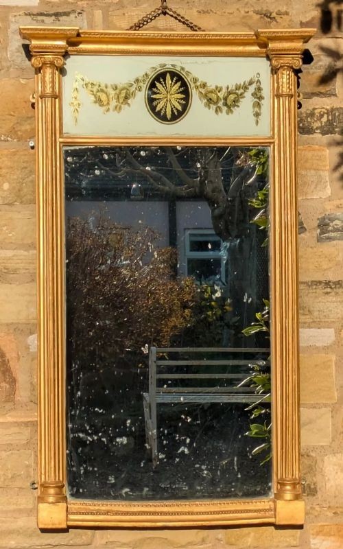 A tall rectangular Regency giltwood pier mirror featuring fluted side columns, an architectural pediment, and an upper verre eglomise panel with gilded swags.