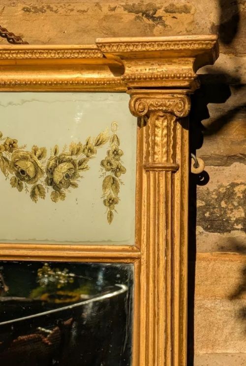 A tall rectangular Regency giltwood pier mirror featuring fluted side columns, an architectural pediment, and an upper verre eglomise panel with gilded swags. View II
