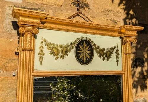 A tall rectangular Regency giltwood pier mirror featuring fluted side columns, an architectural pediment, and an upper verre eglomise panel with gilded swags. View IV