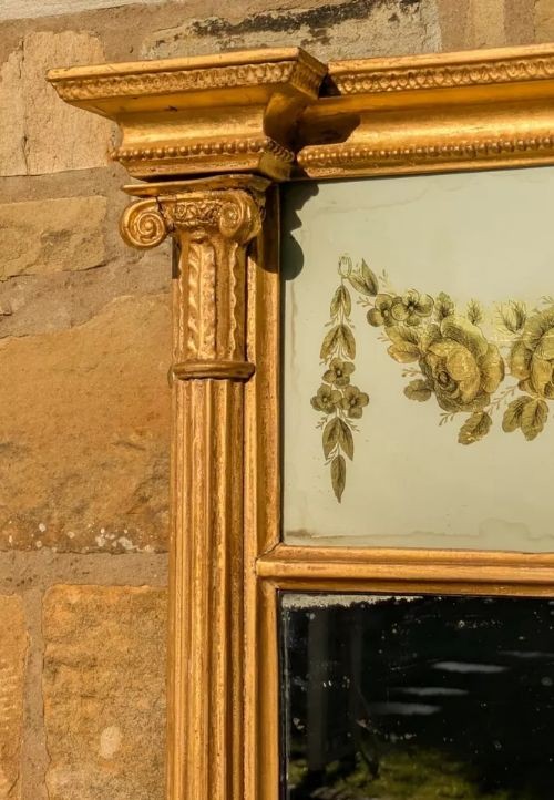 A tall rectangular Regency giltwood pier mirror featuring fluted side columns, an architectural pediment, and an upper verre eglomise panel with gilded swags. View V
