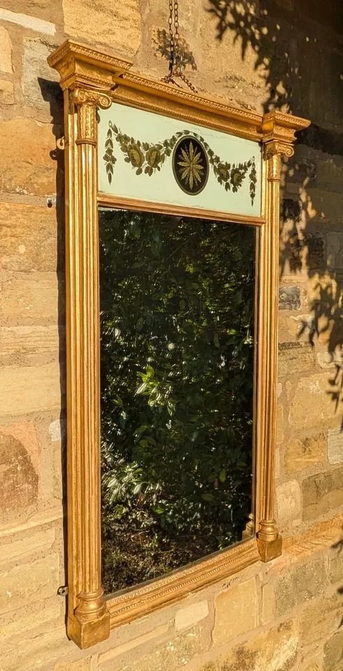 A tall rectangular Regency giltwood pier mirror featuring fluted side columns, an architectural pediment, and an upper verre eglomise panel with gilded swags. View VI