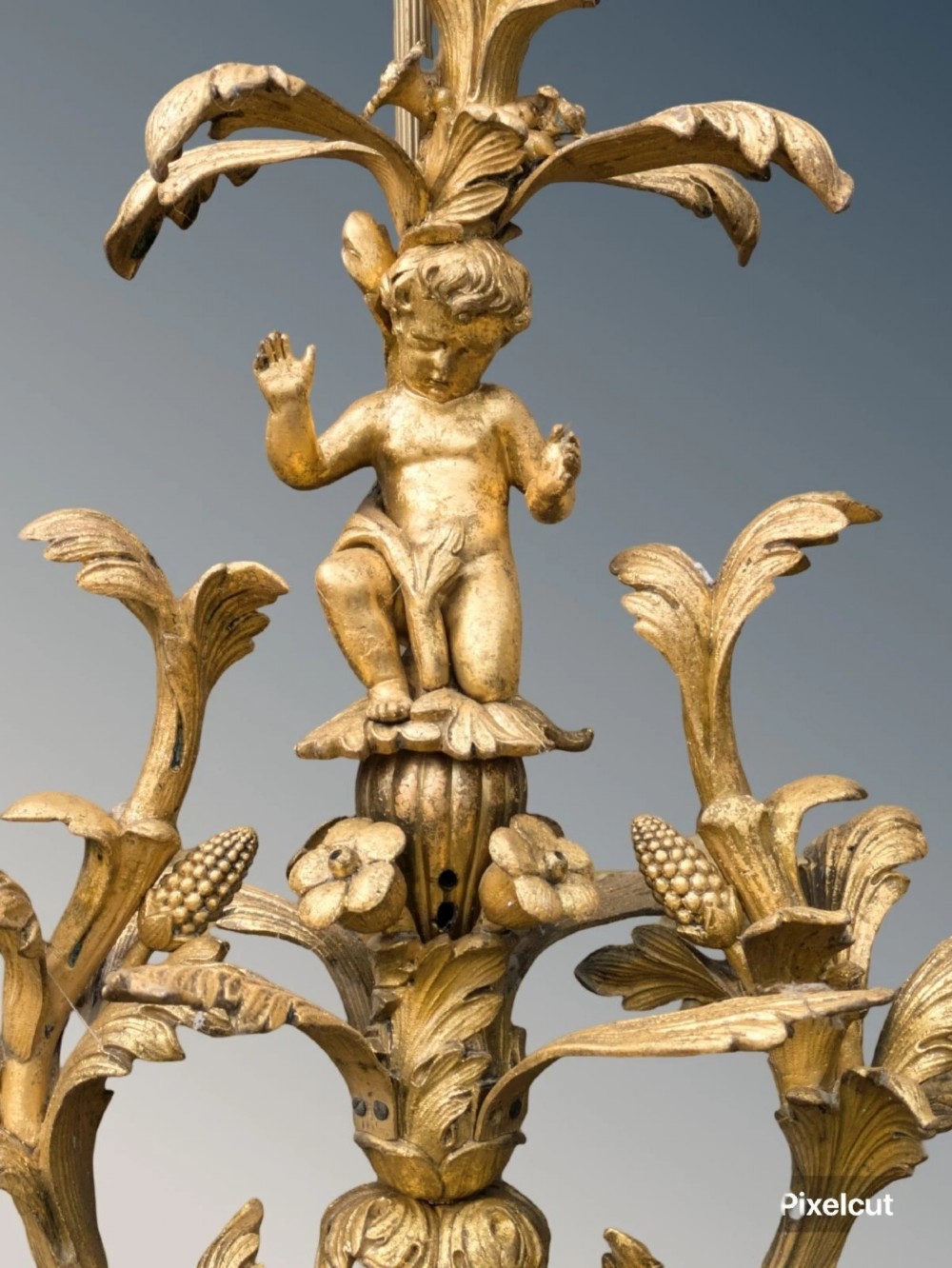 An ornate gilt bronze table lamp featuring a sculpted cherub figure on a floral cast base with a pleated pink silk shade. View V