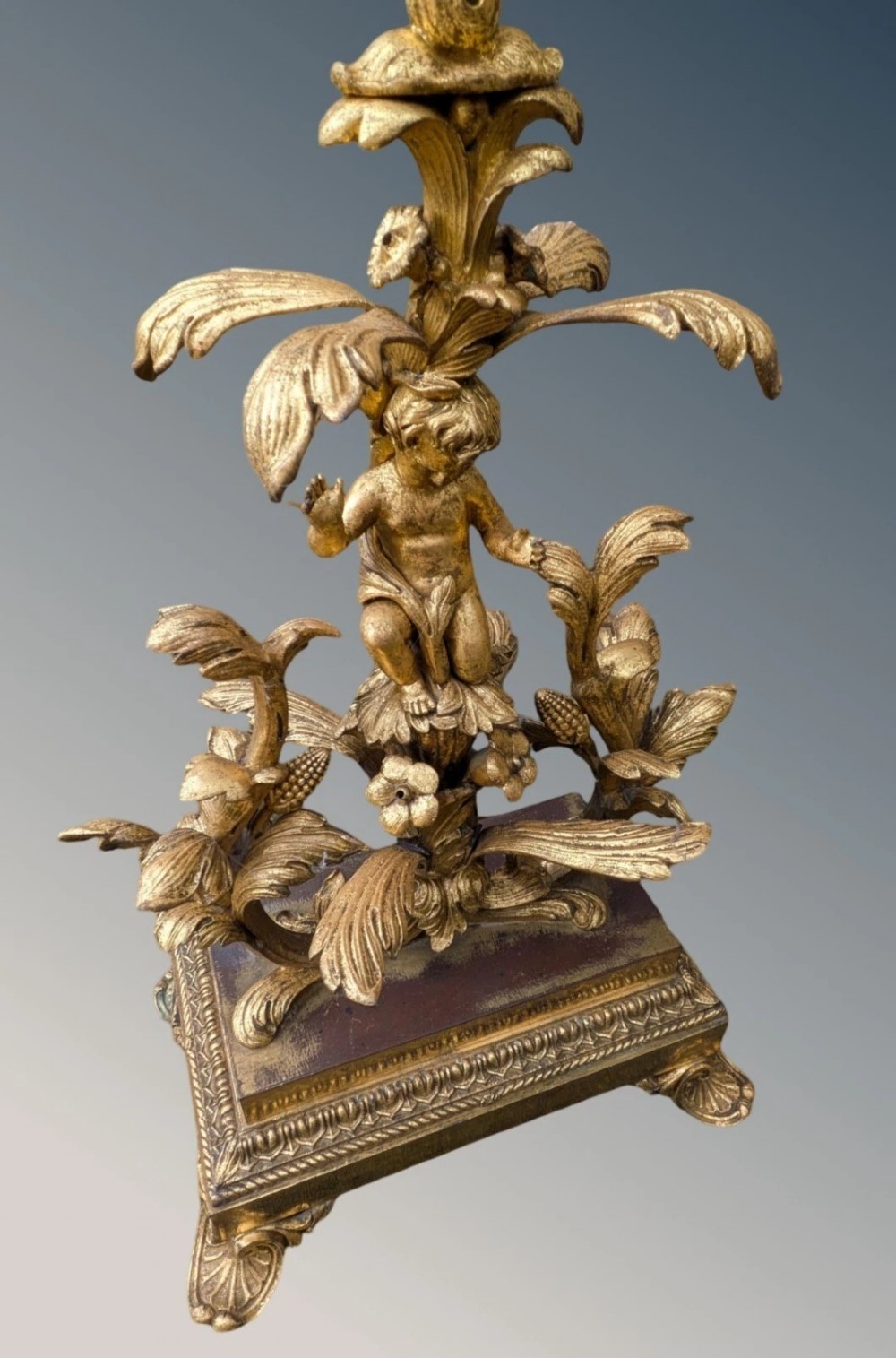 An ornate gilt bronze table lamp featuring a sculpted cherub figure on a floral cast base with a pleated pink silk shade. View VI
