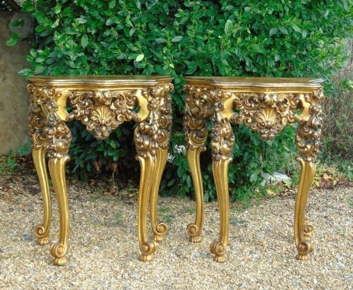 A pair of ornate Spanish giltwood console tables featuring deeply carved shell aprons and cabriole legs resting on scroll feet.