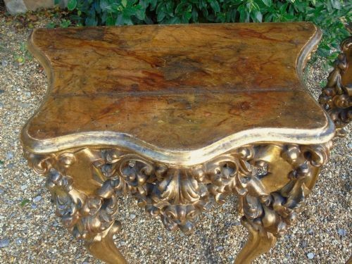 A pair of ornate Spanish giltwood console tables featuring deeply carved shell aprons and cabriole legs resting on scroll feet. View IX