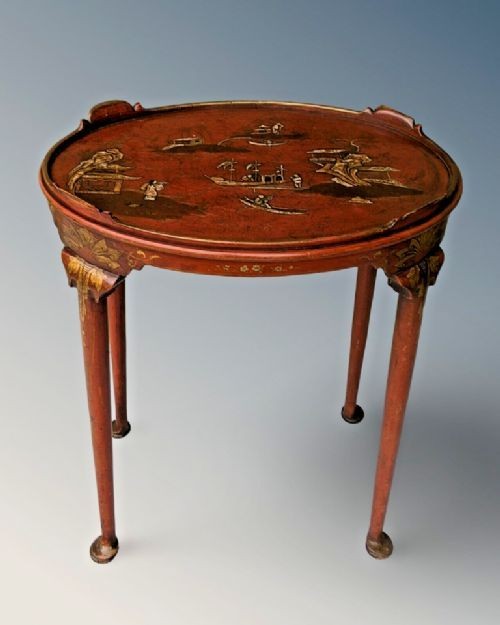 An oval antique red lacquer side table featuring hand-painted gold chinoiserie narrative scenes on the surface and slender legs.