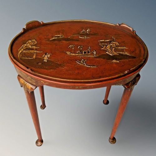 An oval antique red lacquer side table featuring hand-painted gold chinoiserie narrative scenes on the surface and slender legs. View V
