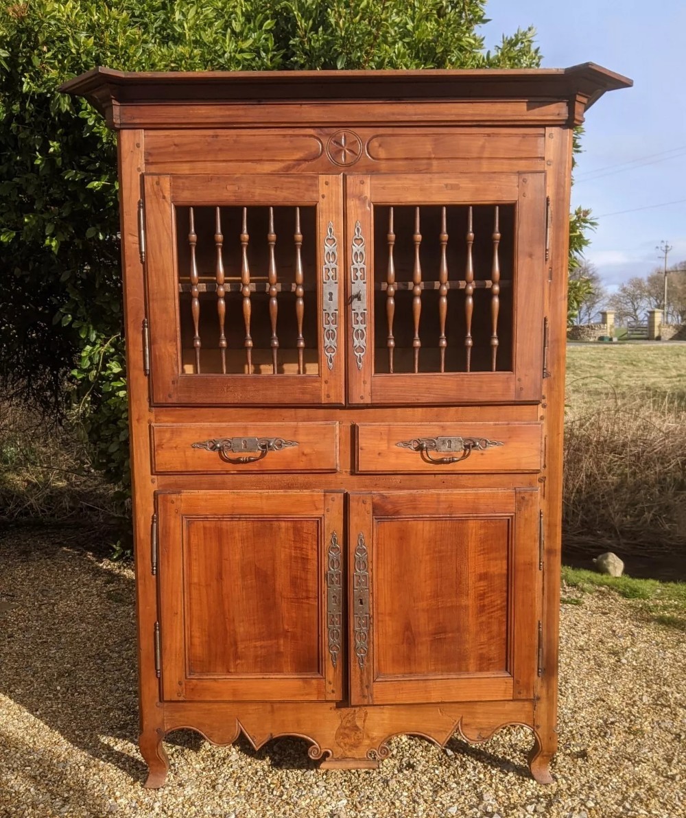 A French provincial fruitwood pantry cabinet featuring upper spindle-front doors, two central drawers with steel handles, lower solid panel doors, and carved cabriole feet.