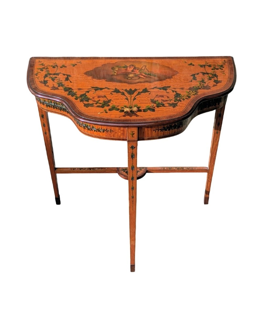 A Regency satinwood side table with a shaped top decorated with hand-painted floral swags and a central cherub medallion, supported by slim tapering legs.