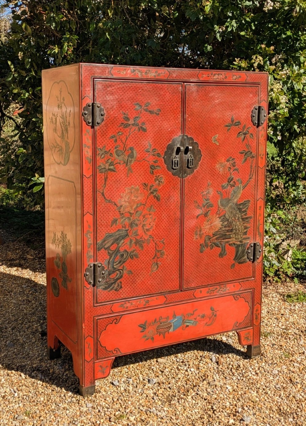 A red lacquered two-door Chinese cabinet decorated with black and gold hand-painted floral and bird motifs, supported on straight block feet and fitted with brass hardware.