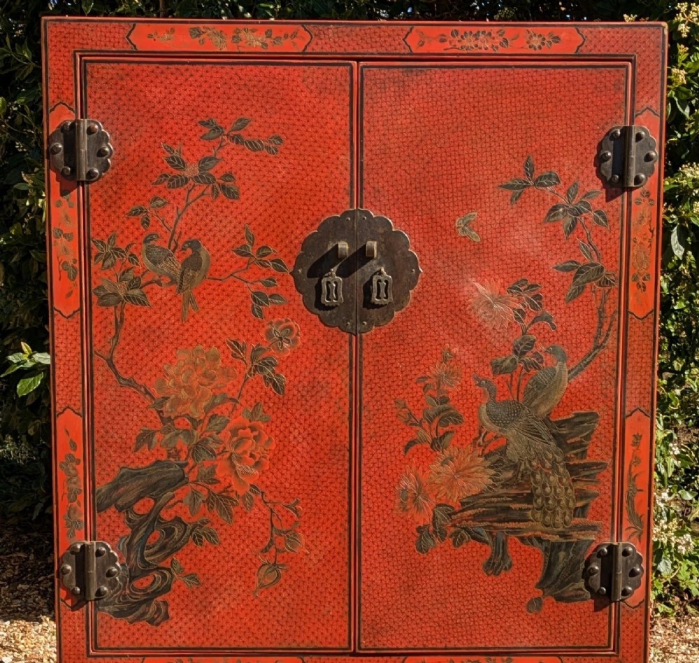 A red lacquered two-door Chinese cabinet decorated with black and gold hand-painted floral and bird motifs, supported on straight block feet and fitted with brass hardware. View IV