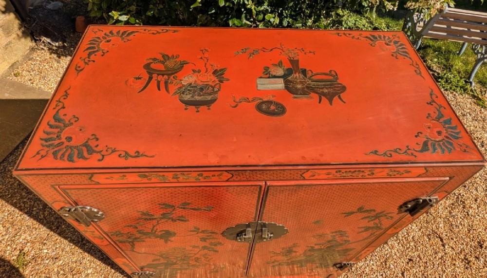 A red lacquered two-door Chinese cabinet decorated with black and gold hand-painted floral and bird motifs, supported on straight block feet and fitted with brass hardware. View VIII