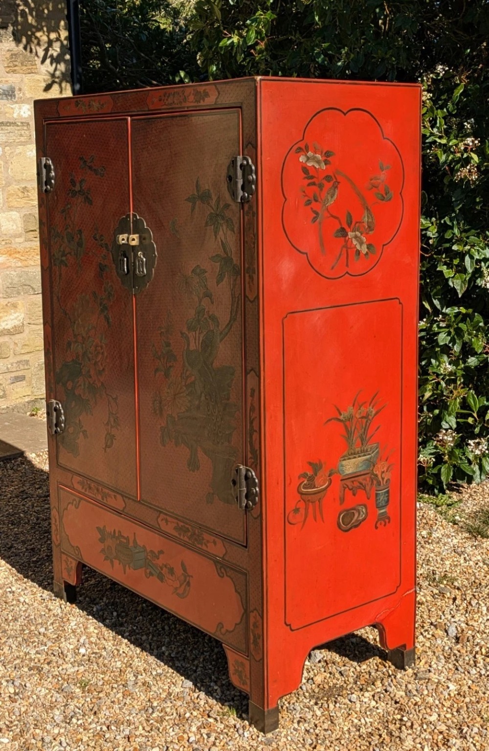 A red lacquered two-door Chinese cabinet decorated with black and gold hand-painted floral and bird motifs, supported on straight block feet and fitted with brass hardware. View X