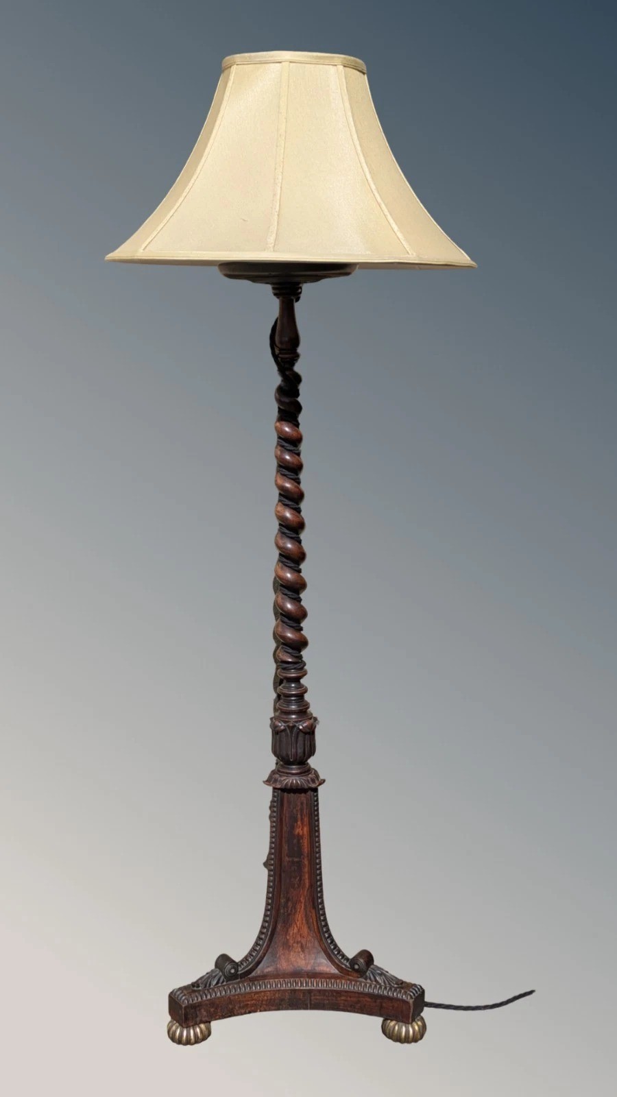 A dark rosewood Regency standard lamp featuring a barley twist column, a carved triform base with brass feet, and a cream fabric shade.