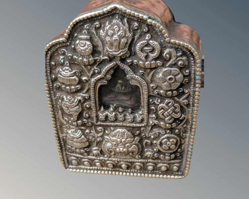 An arched Tibetan Gau prayer shrine featuring an intricately embossed silver metal front panel mounted on a copper casing with side loops. View IV