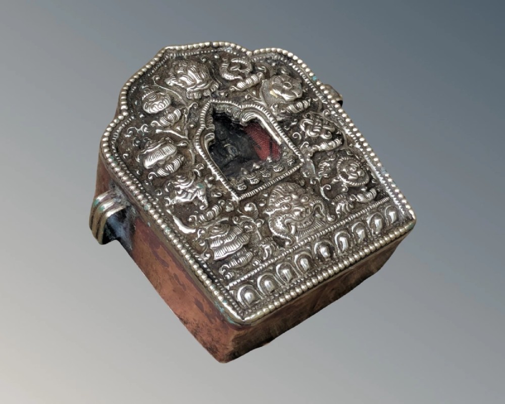 An arched Tibetan Gau prayer shrine featuring an intricately embossed silver metal front panel mounted on a copper casing with side loops. View V