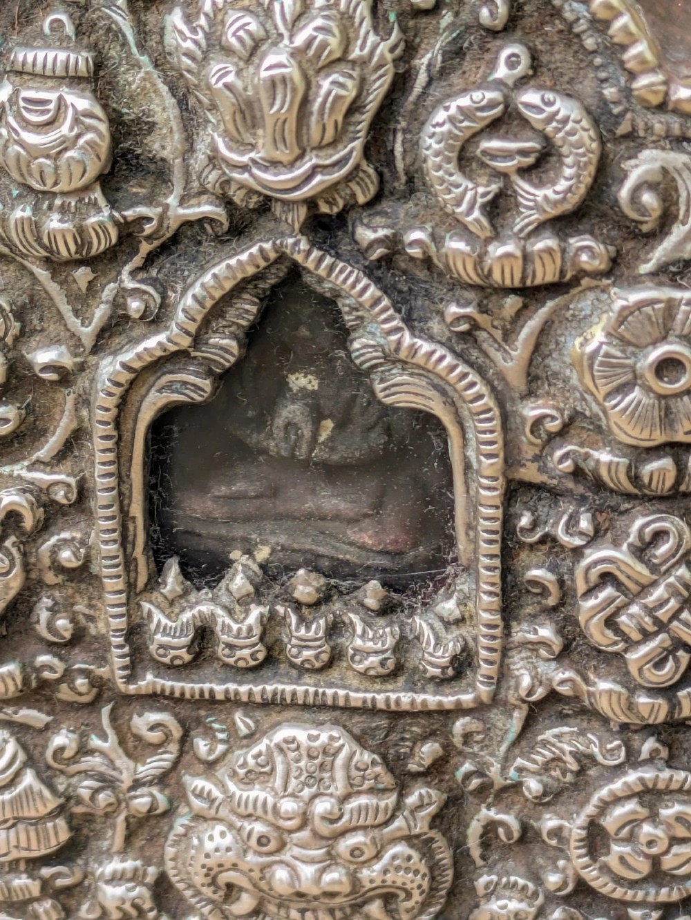 An arched Tibetan Gau prayer shrine featuring an intricately embossed silver metal front panel mounted on a copper casing with side loops. View VI