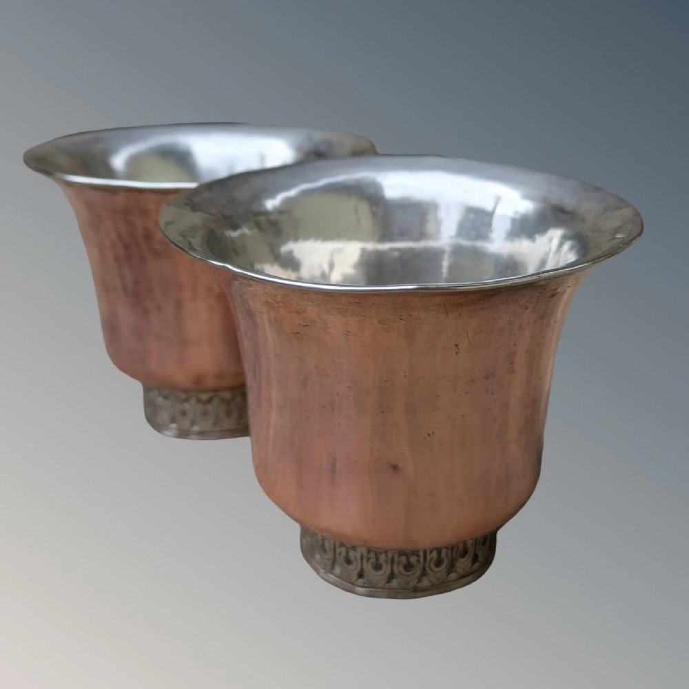 A pair of antique Tibetan flared drinking vessels with hand-hammered copper bodies, silver-lined interiors, and carved silver bases.
