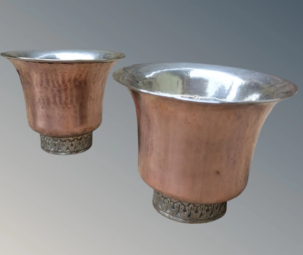 A pair of antique Tibetan flared drinking vessels with hand-hammered copper bodies, silver-lined interiors, and carved silver bases. View V