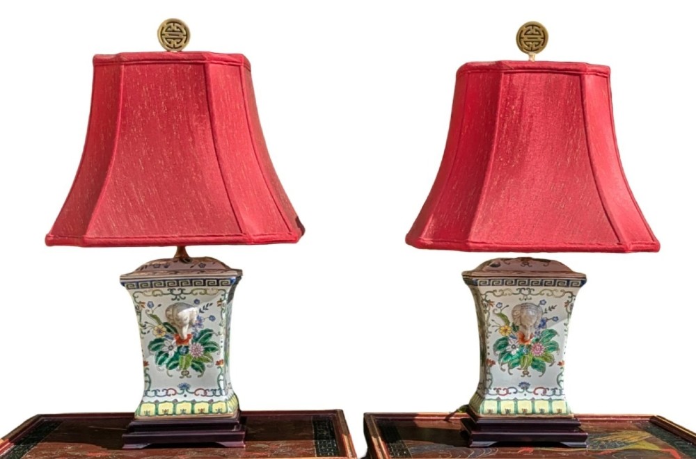 A pair of Chinese porcelain table lamps featuring hand-painted floral motifs and relief elephant details, topped with red silk shades.