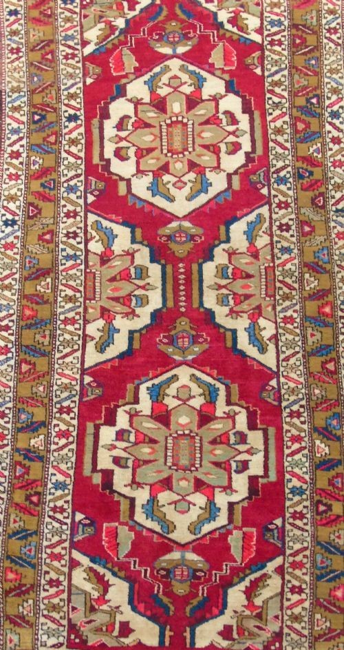 A hand-knotted Heriz carpet runner featuring geometric ivory medallions set against a deep red ground framed by multi-coloured decorative borders.