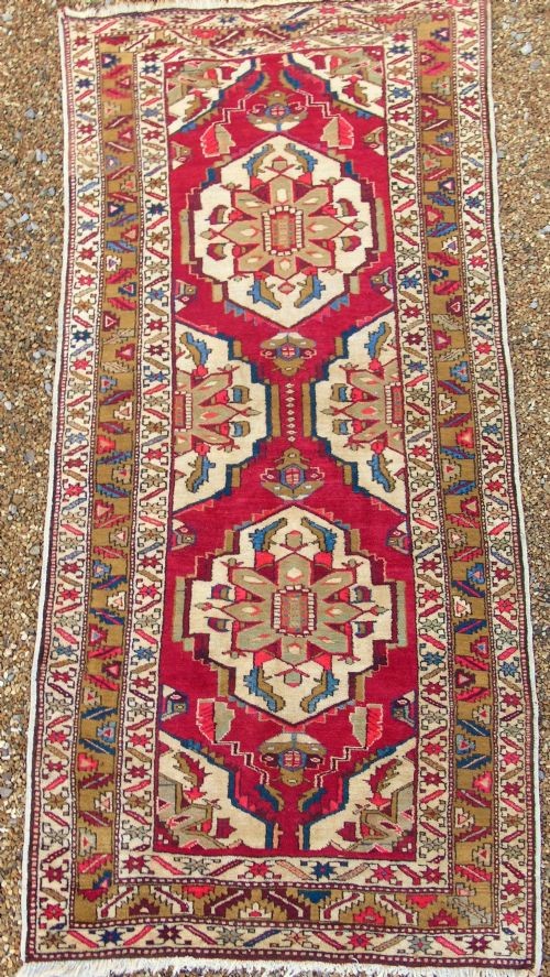 A hand-knotted Heriz carpet runner featuring geometric ivory medallions set against a deep red ground framed by multi-coloured decorative borders. View III