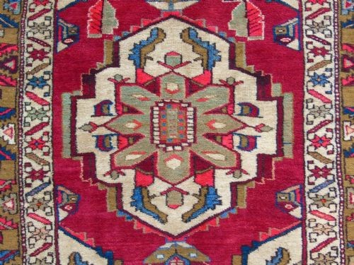 A hand-knotted Heriz carpet runner featuring geometric ivory medallions set against a deep red ground framed by multi-coloured decorative borders. View IV