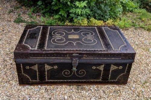 A dark brown leather rectangular coffer decorated with brass stud patterns, scrolling motifs, and a central metal latch. View X