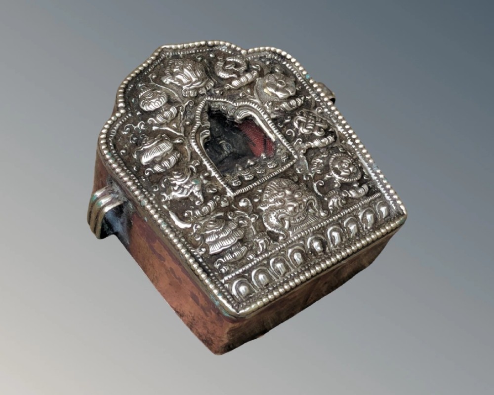 A Tibetan silver Gau travelling prayer box featuring embossed repousse ornamentation, an arched central niche housing a deity, and a copper casing. View III