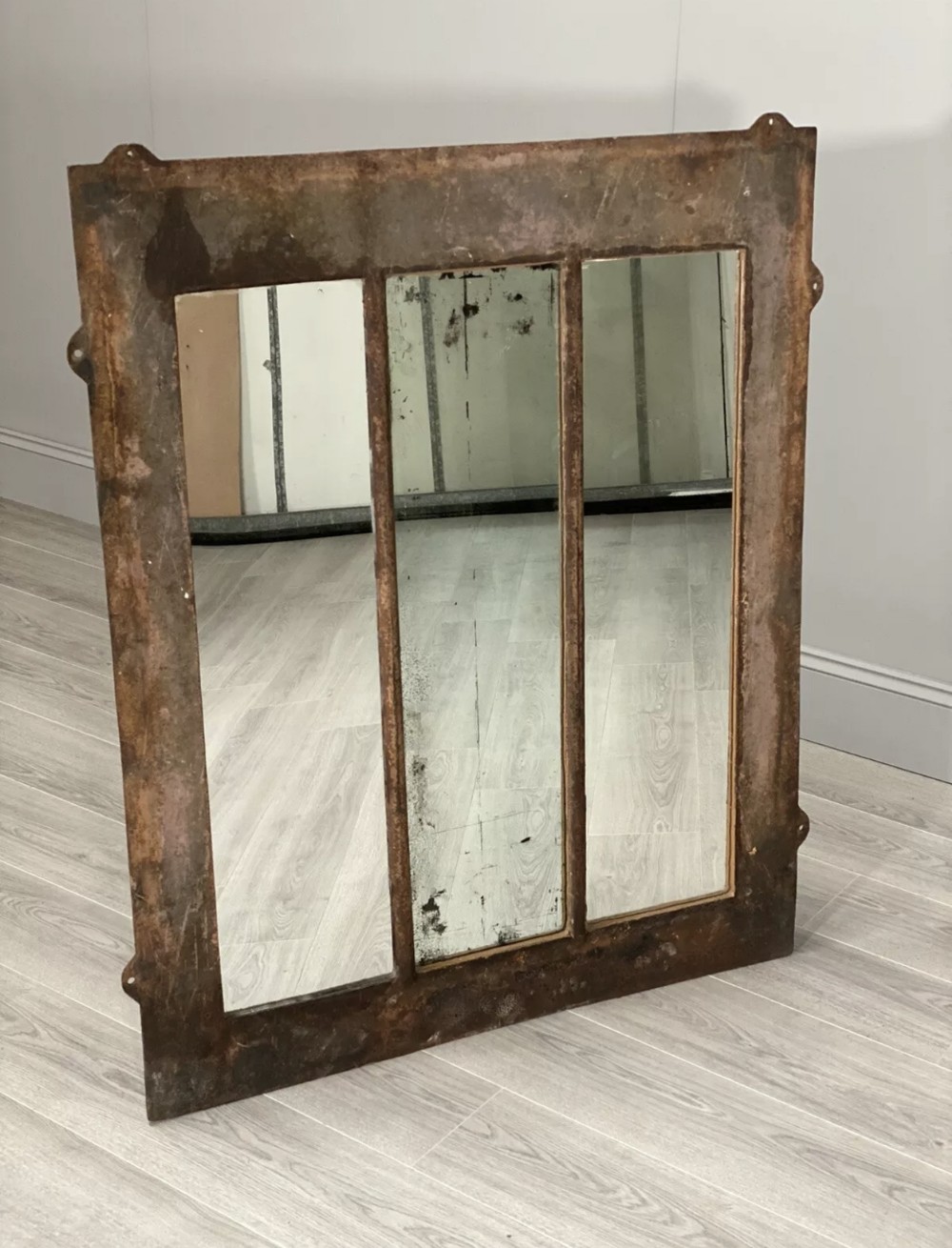 A large rectangular cast iron mirror with a rusted patina and internal window frame grid divisions.