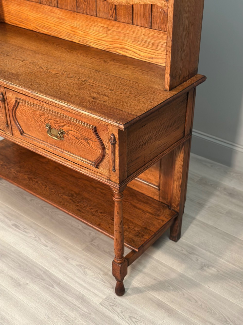 An antique oak Welsh dresser featuring a three-tier open plate rack above two moulded drawers with brass handles and a lower open potboard shelf supported by turned front legs. View III