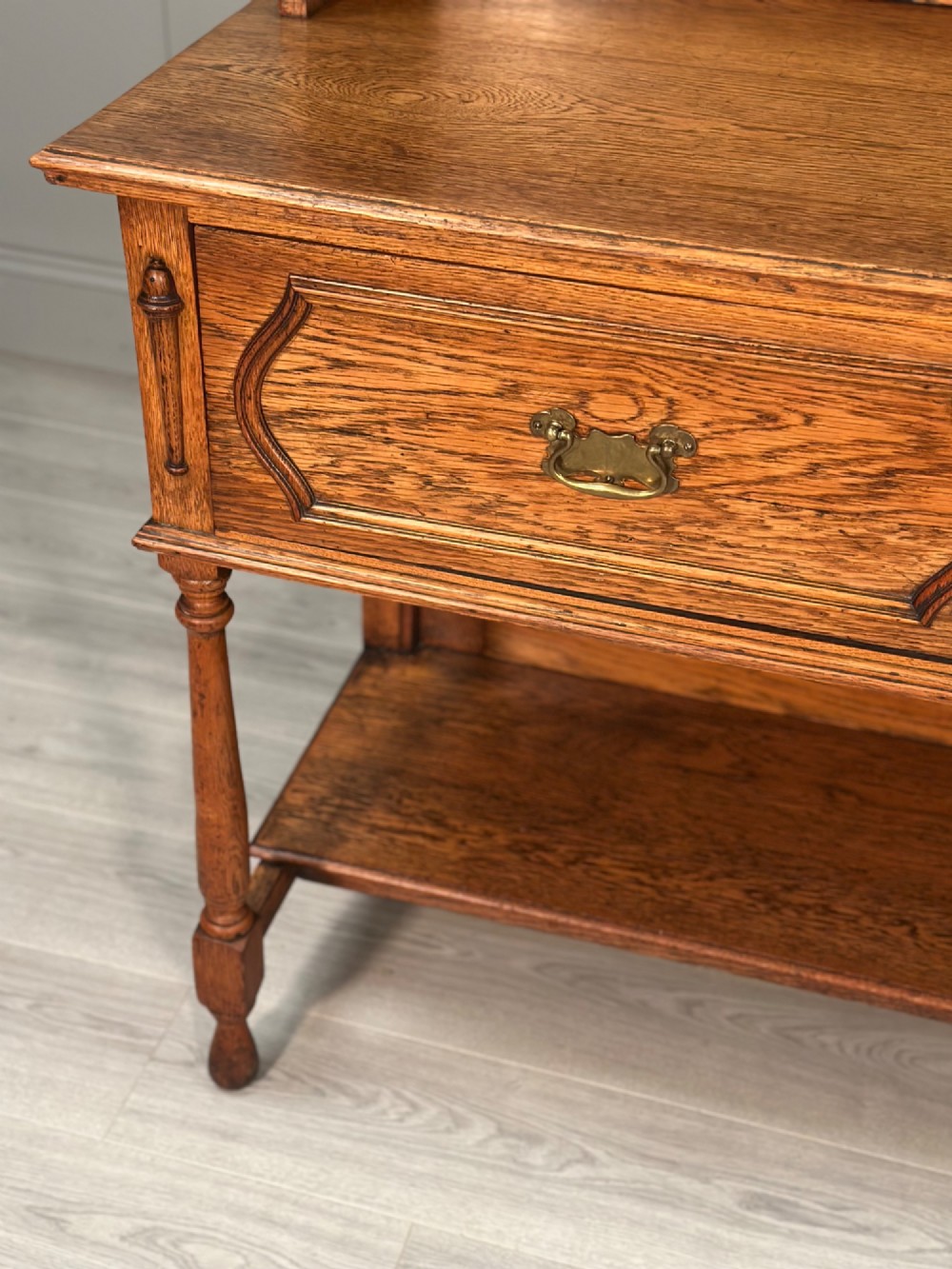 An antique oak Welsh dresser featuring a three-tier open plate rack above two moulded drawers with brass handles and a lower open potboard shelf supported by turned front legs. View V